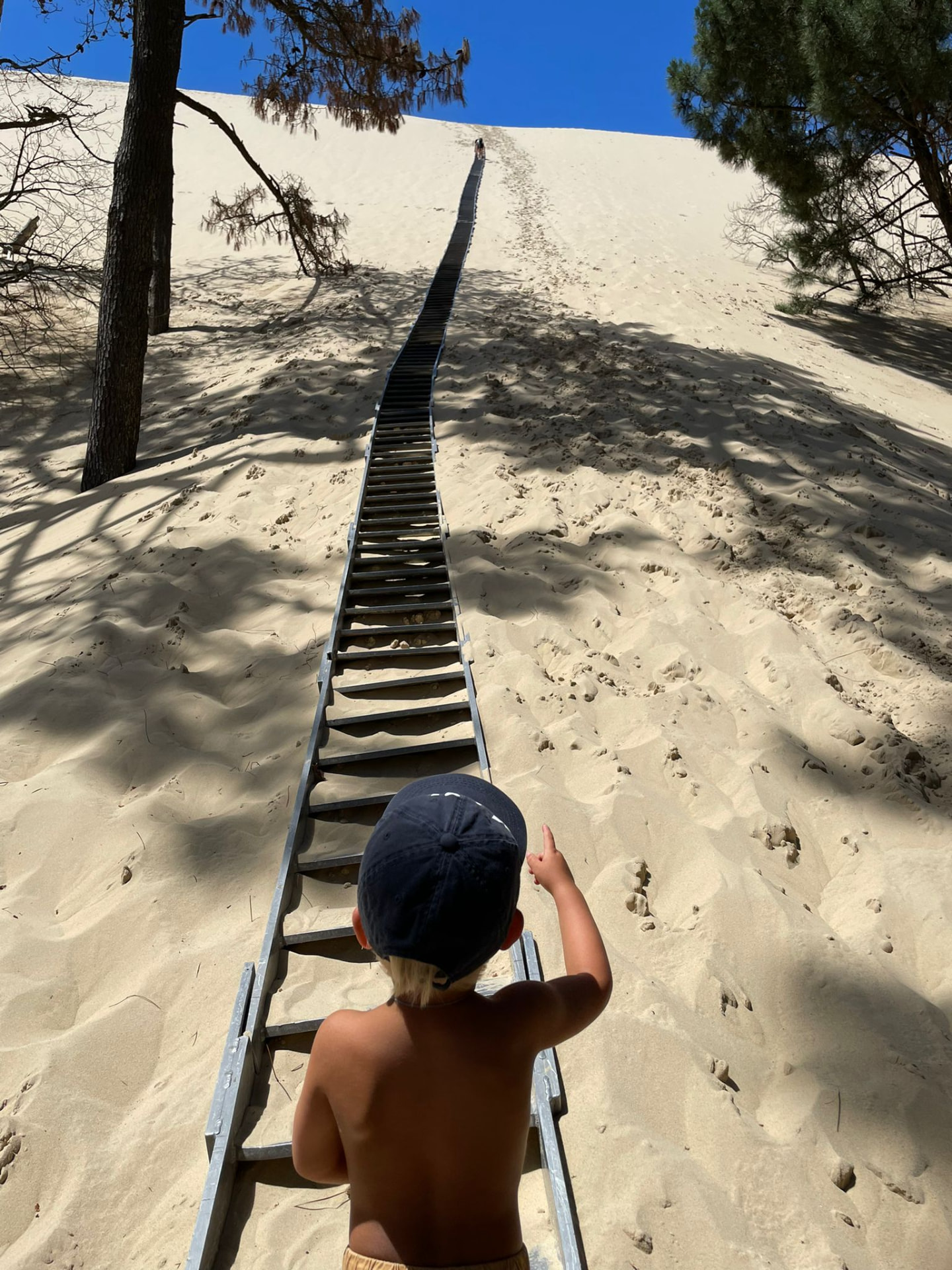 Kind zeigt die lange Leiter eine grosse Sanddüne hinauf