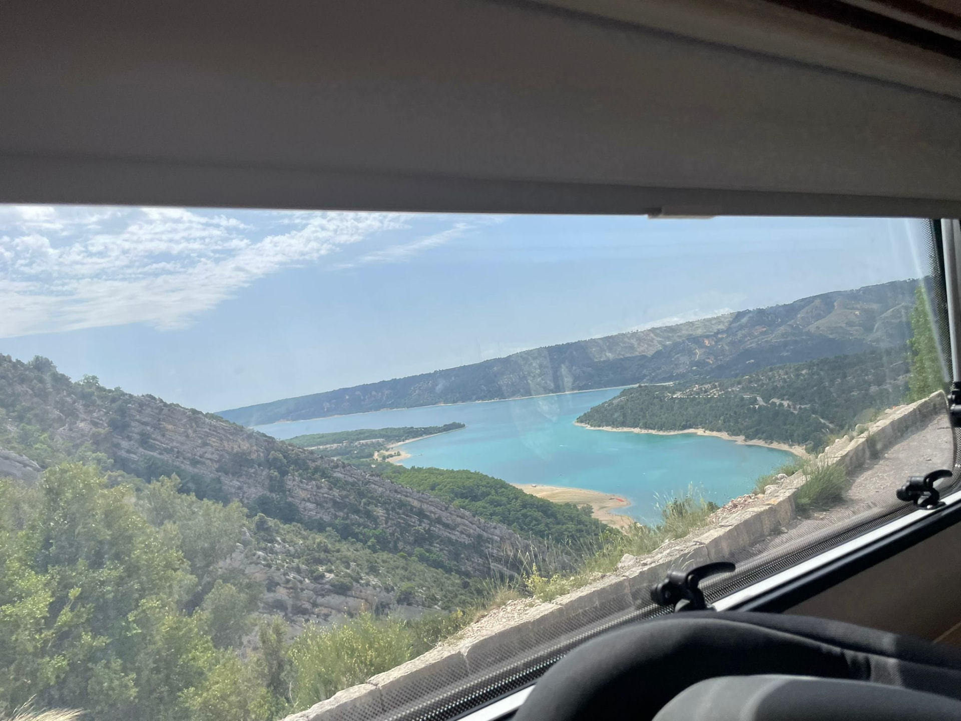 Blick aus dem Wohnmobilfenster auf einen türkisblauen See zwischen Bergen